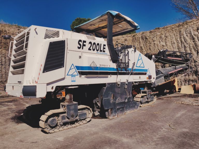 Macchina fresatrice bianca su cingoli in un cantiere.
