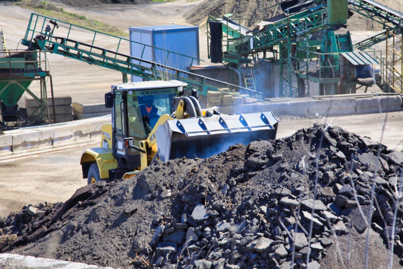 Ruspa gialla sposta cumulo di asfalto in cantiere.