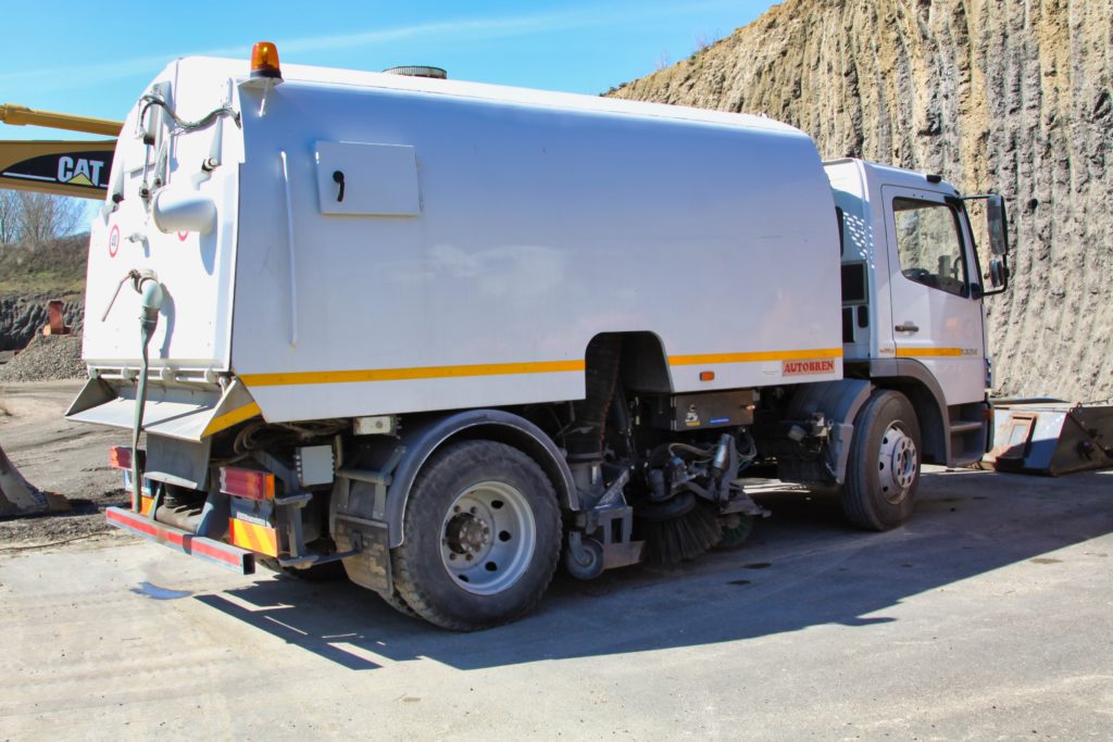 Camion spazzatrice bianco parcheggiato su strada sterrata.