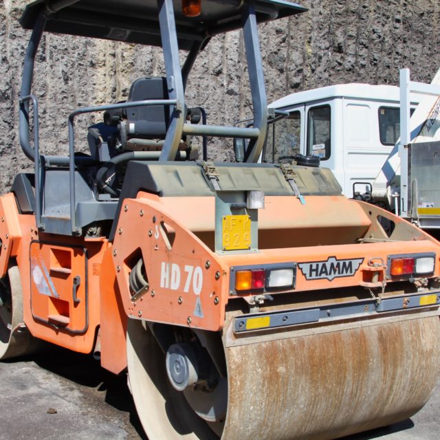 Rullo compressore arancione parcheggiato accanto a un camion.