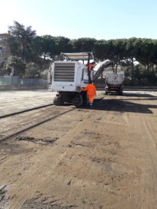 Operai con macchinari lavorano su strada sterrata.